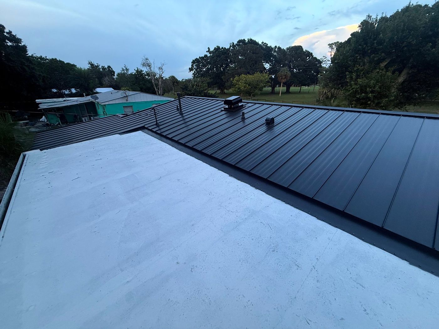 Finished black standing-seam metal roof at dusk beside a flat section